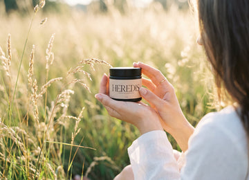 Woman holding a jar of Heredis Vanilla Pine Tallow Lotion in a golden meadow